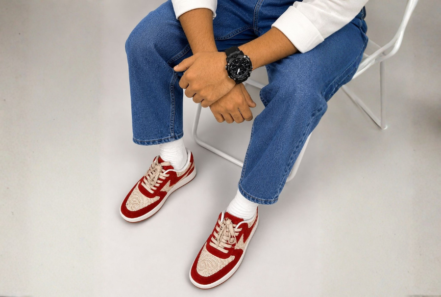 Seated person in blue jeans wearing red and white NAAW sneakers